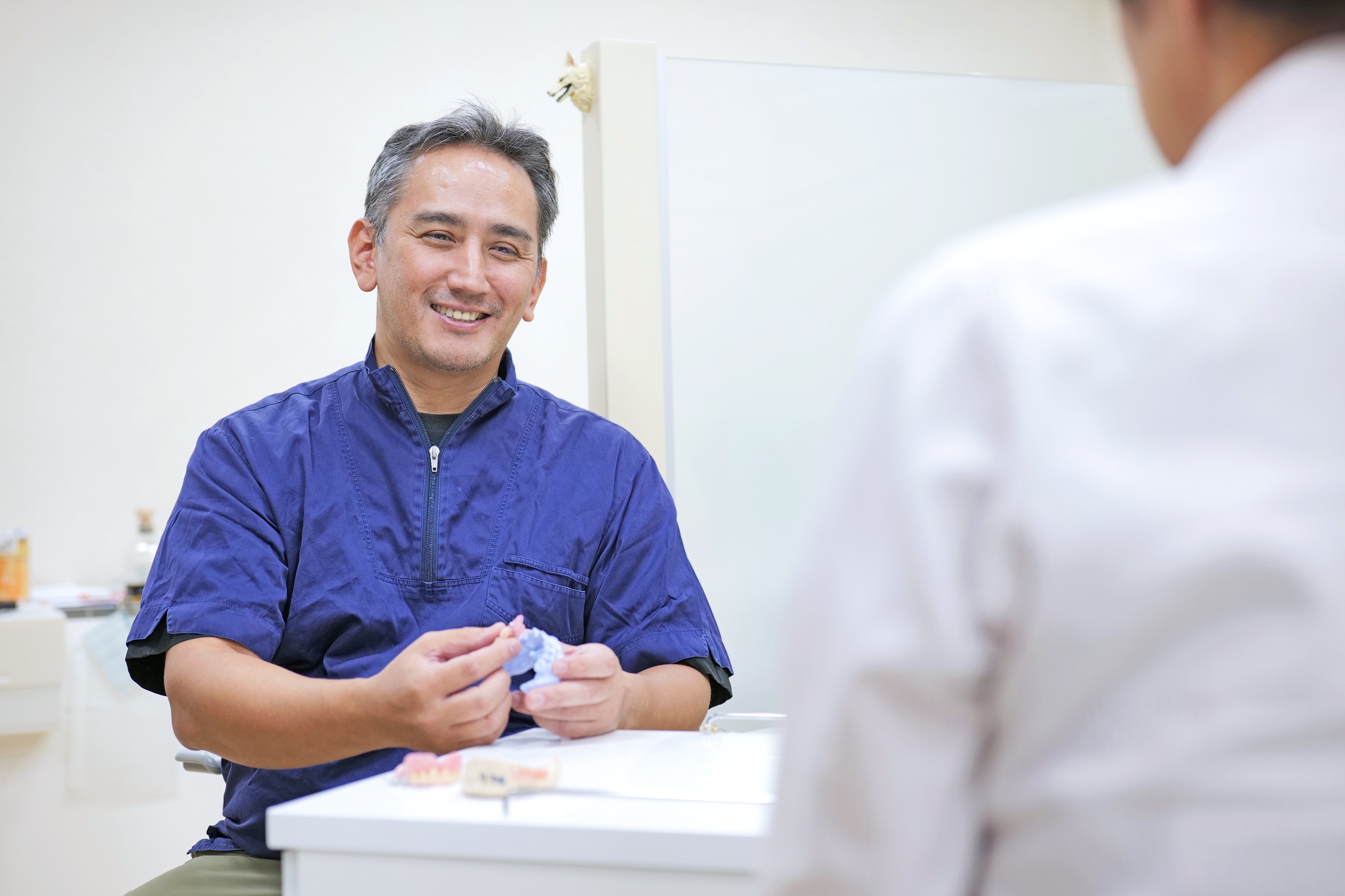 入れ歯の模型を手に患者さんと笑顔で相談する理事長