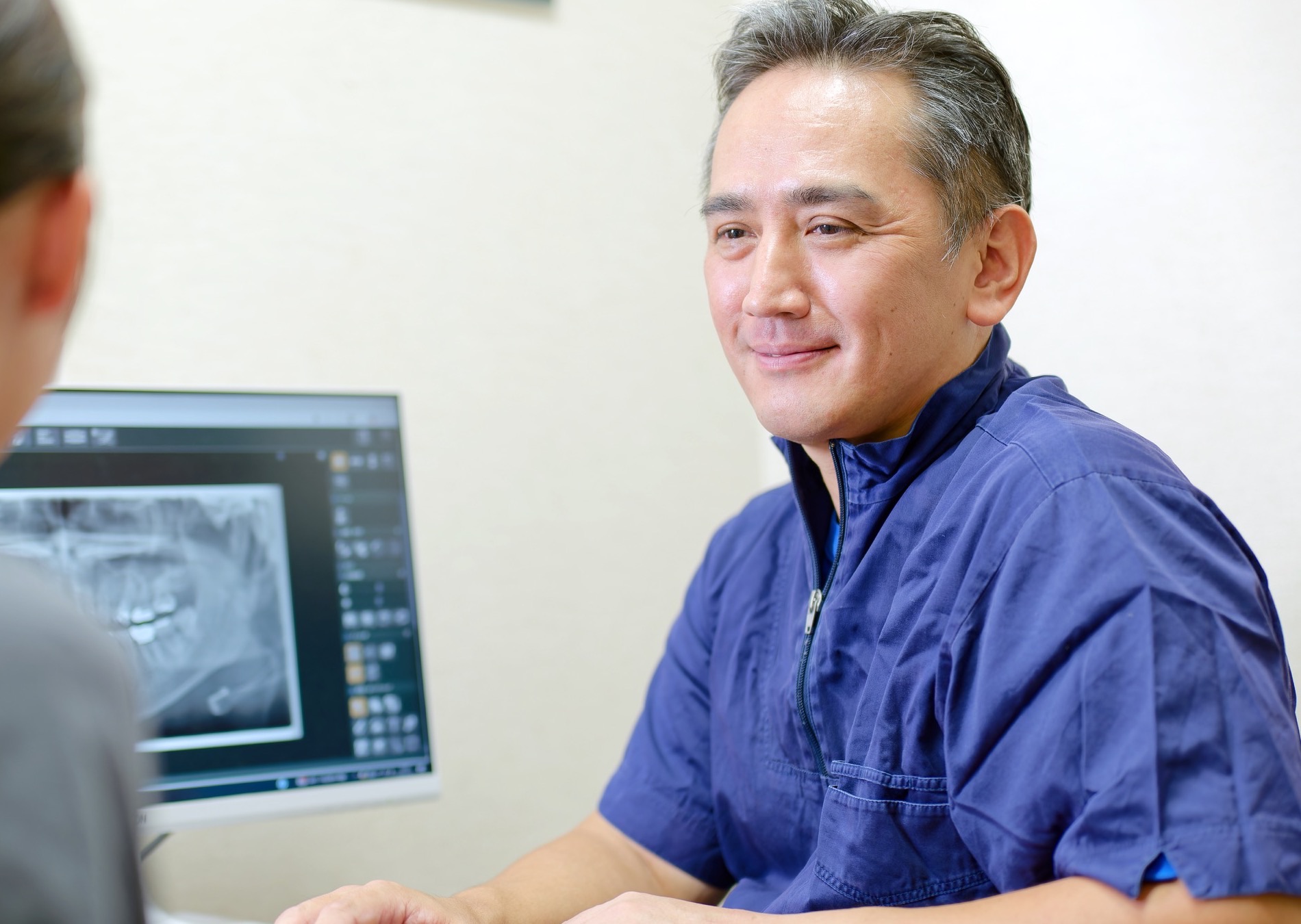 患者さんの肩越しに理事長がレントゲン画像を確認しながら相談に応じる様子